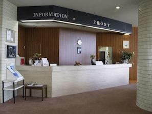 A reception desk with a sign that reads 'INFORMATION FRONT' and a counter with a plant and a vase.