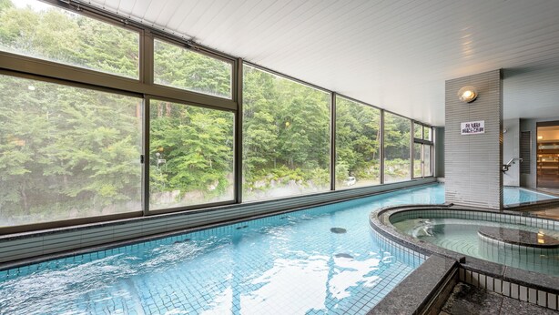 A swimming pool with large windows offering a view of a forested area. - Hotel Tagawa (Yamanouchi)