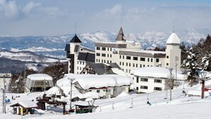 A large hotel with multiple buildings, ski lifts, and snow-covered mountains in the background. - Hotel Tagawa (Yamanouchi)