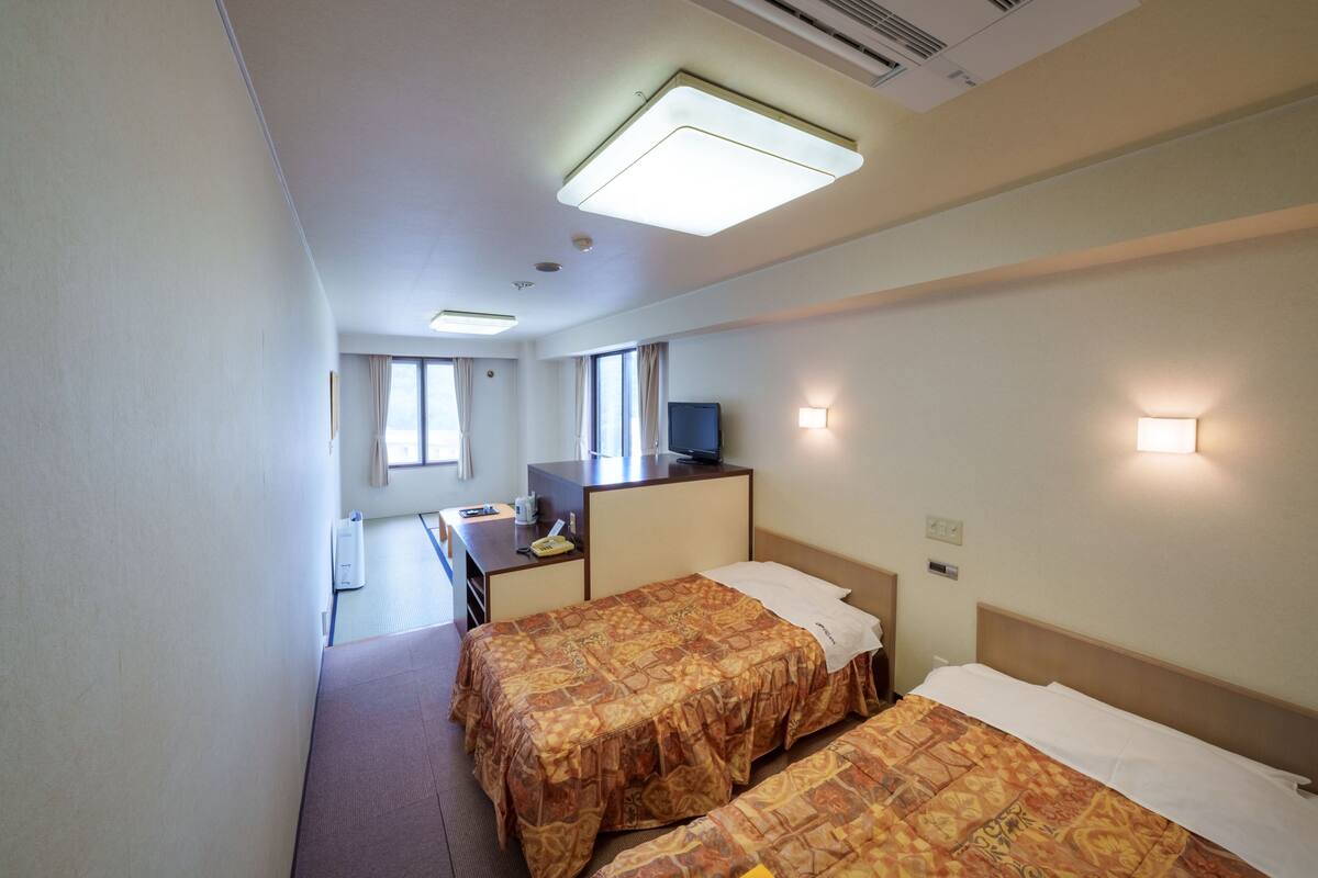 Ein Hotelzimmer mit zwei Betten, einem Schreibtisch, einem Fernseher und einem Fenster.