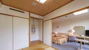 A hotel room with tatami flooring, a bed with a floral bedspread, a desk with a computer, a chair, and a small table. - Hotel Tagawa (Yamanouchi)