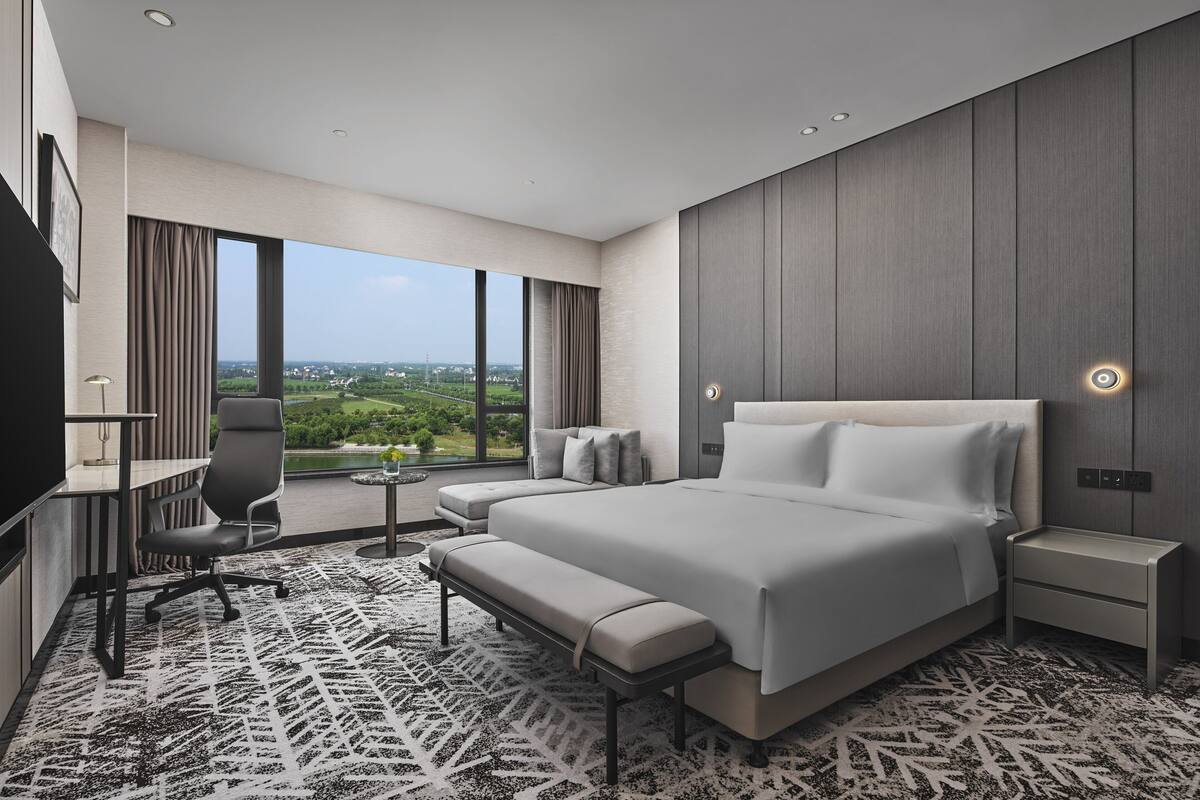 A modern hotel room with a large bed, a desk, and a view of the city.
