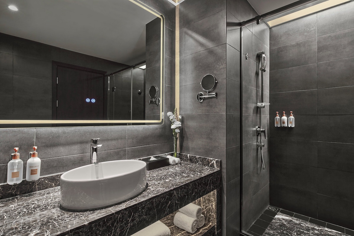 A modern bathroom with a large mirror, a round sink, and a walk-in shower.