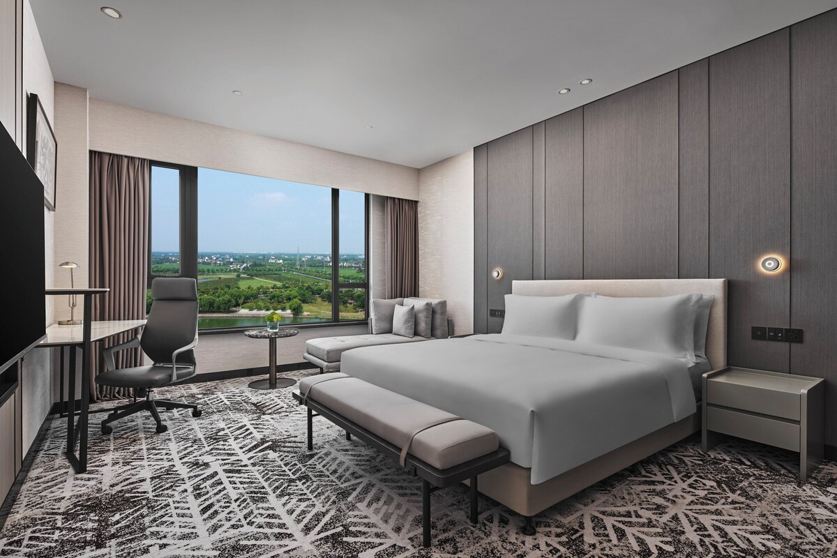 A modern hotel room with a large bed, a desk, and a view of the city.