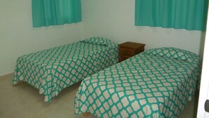 Una habitación pequeña con dos camas individuales, una mesita de noche de madera y un equipo de aire acondicionado en la pared.