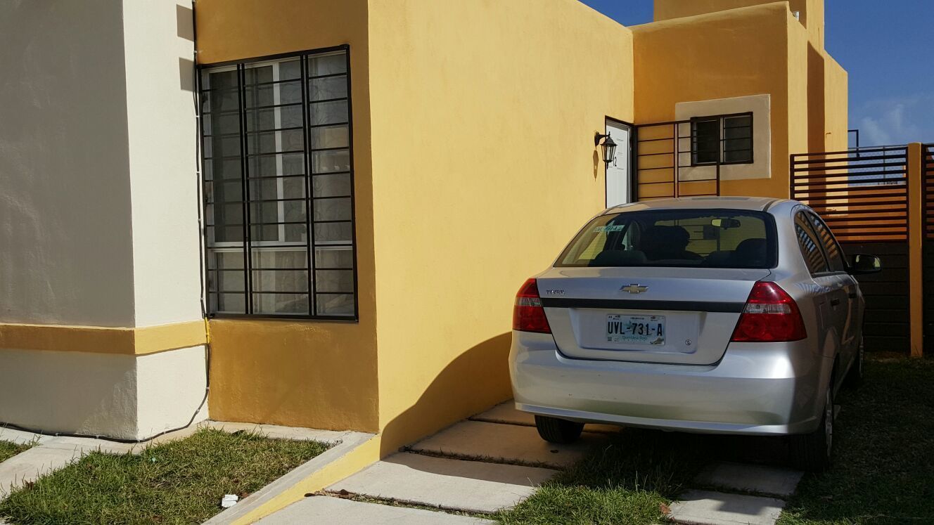 A silver car parked in front of a yellow building with a window and a door.