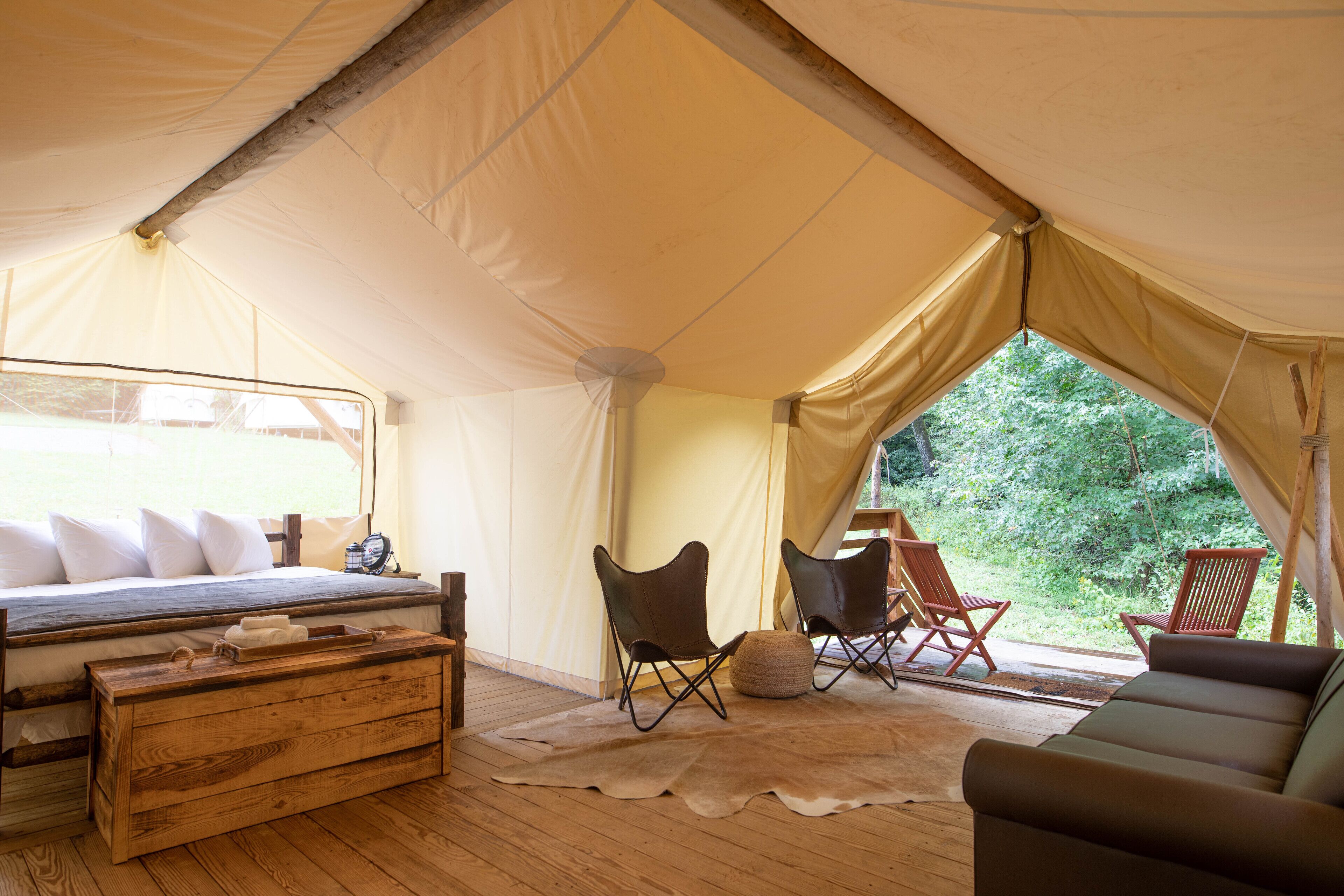Una carpa con una cama, un cofre de madera, dos sillas, un sofá y vistas al verdor.