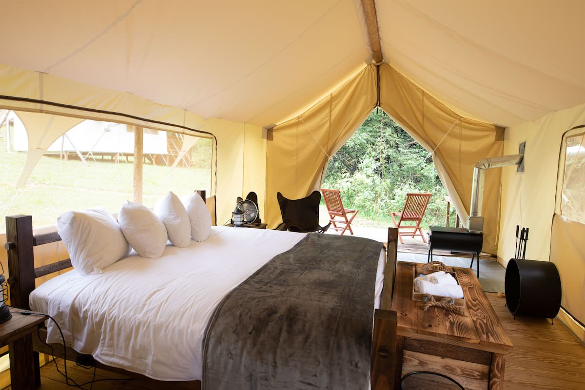 A tented accommodation with a bed, a table, and a chair.