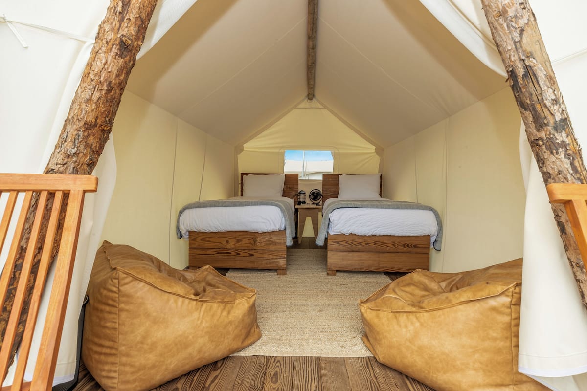 A cozy tented room with two wooden beds, a small table, and two bean bags.
