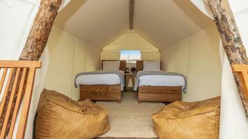Una habitación con tienda de campaña acogedora, con dos camas de madera, una mesita y dos pufs.