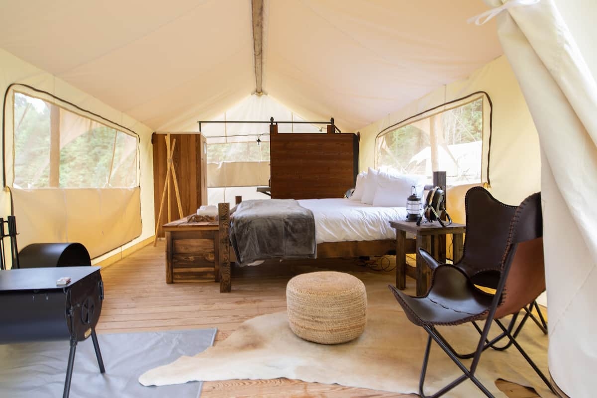 A tented room with a bed, a desk, a chair, and a rug.