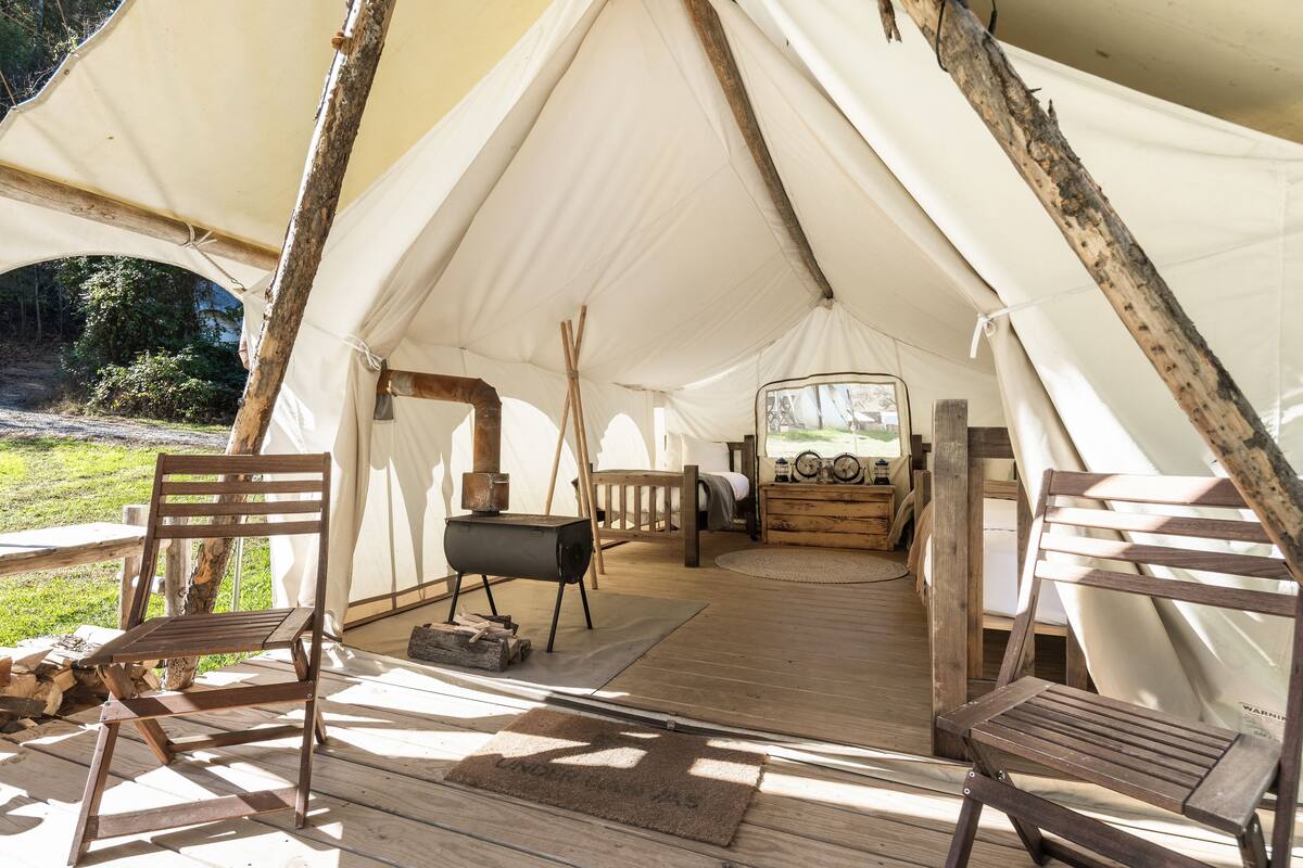 A tent with a wooden deck, a grill, and a surfboard.
