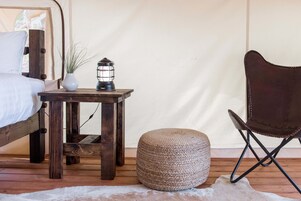 Ein rustikales Schlafzimmer mit einem hölzernen Bett, einem kleinen Tisch mit einer Laterne, einem gewebten Hocker und einem Ledersessel.