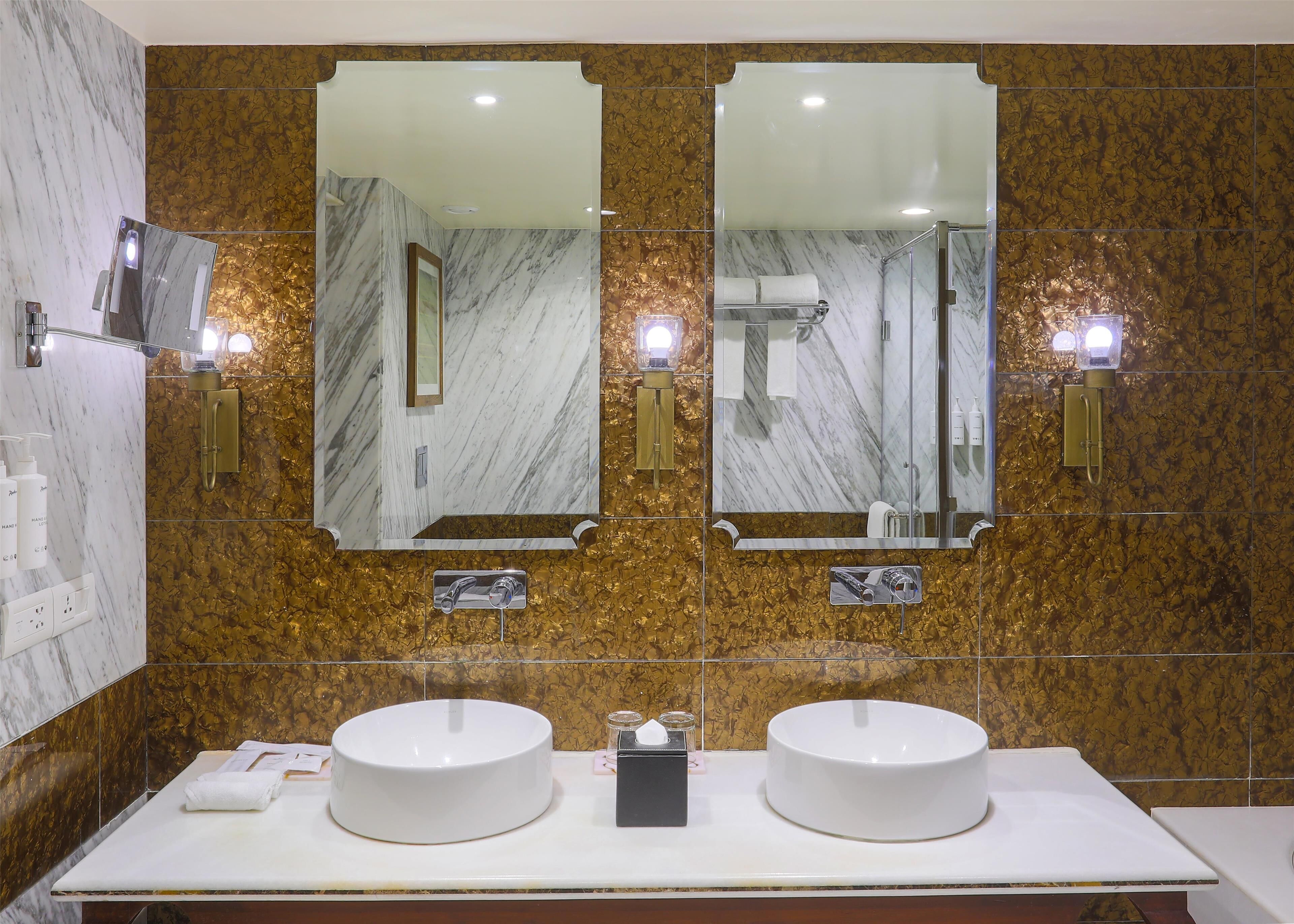 A bathroom with two sinks, a large mirror, and gold-tiled walls.