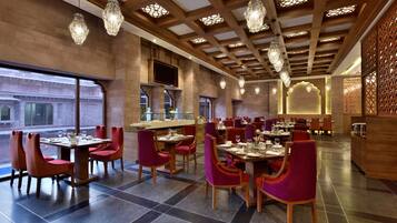 A modern restaurant with wooden ceiling beams, hanging crystal chandeliers, and red upholstered chairs.