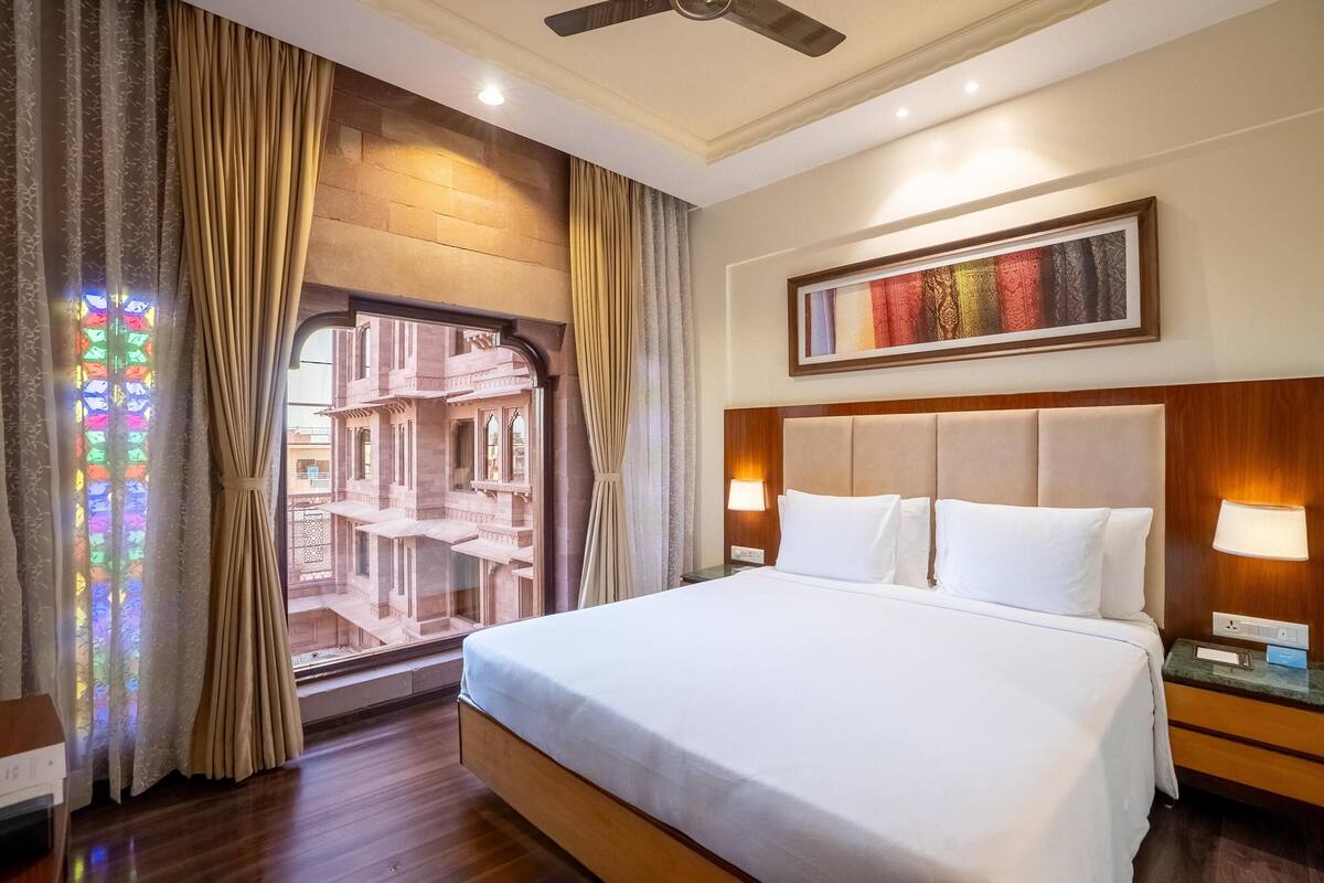 Ein Hotelzimmer mit einem großen Bett, einem Nachttisch, einer Wandlampe und einem fenster mit Vorhängen.