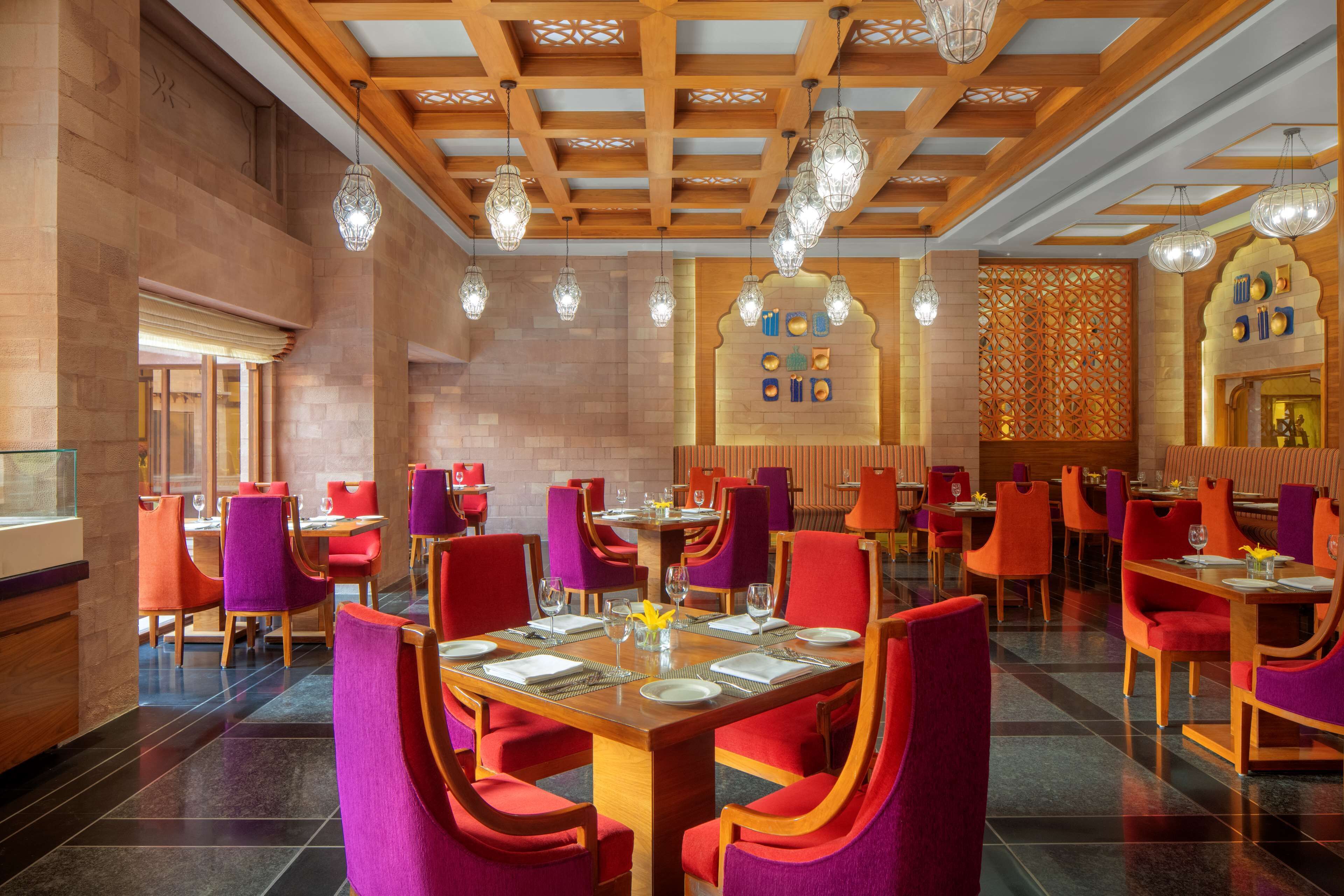 Un restaurante espacioso con vigas de madera en el techo, sillas rojas y púrpuras, y diferentes tipos de mesas.