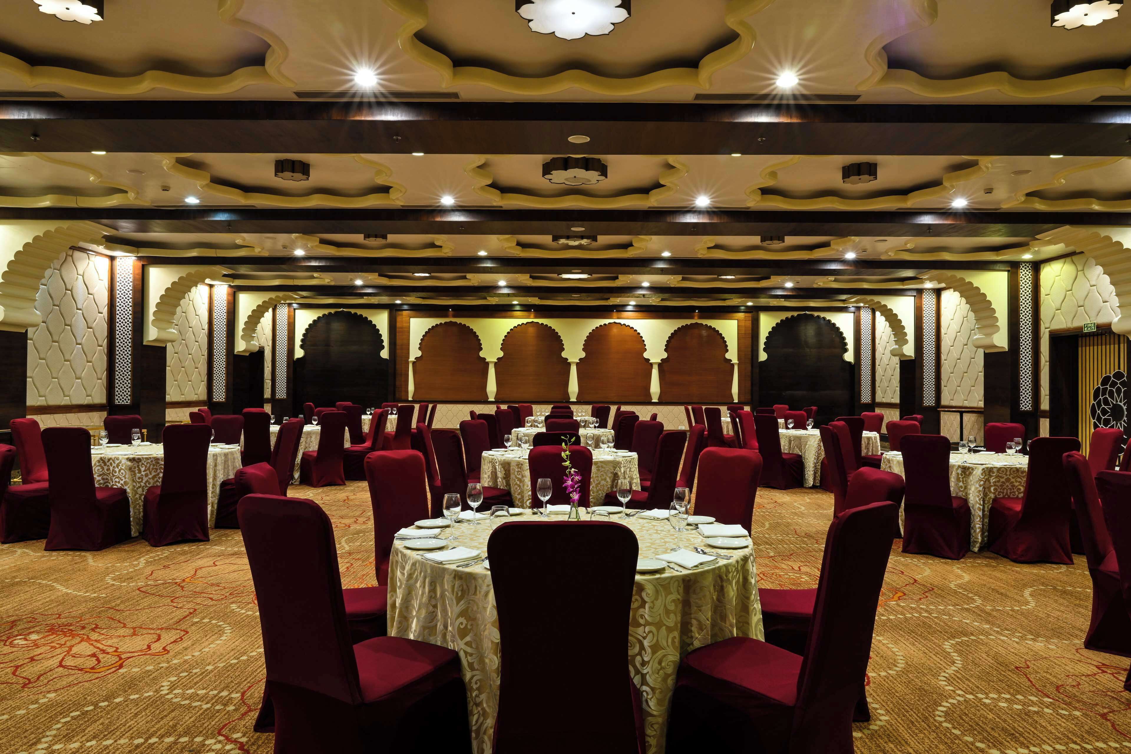A banquet hall with round tables, red chairs, and ornate ceiling design.