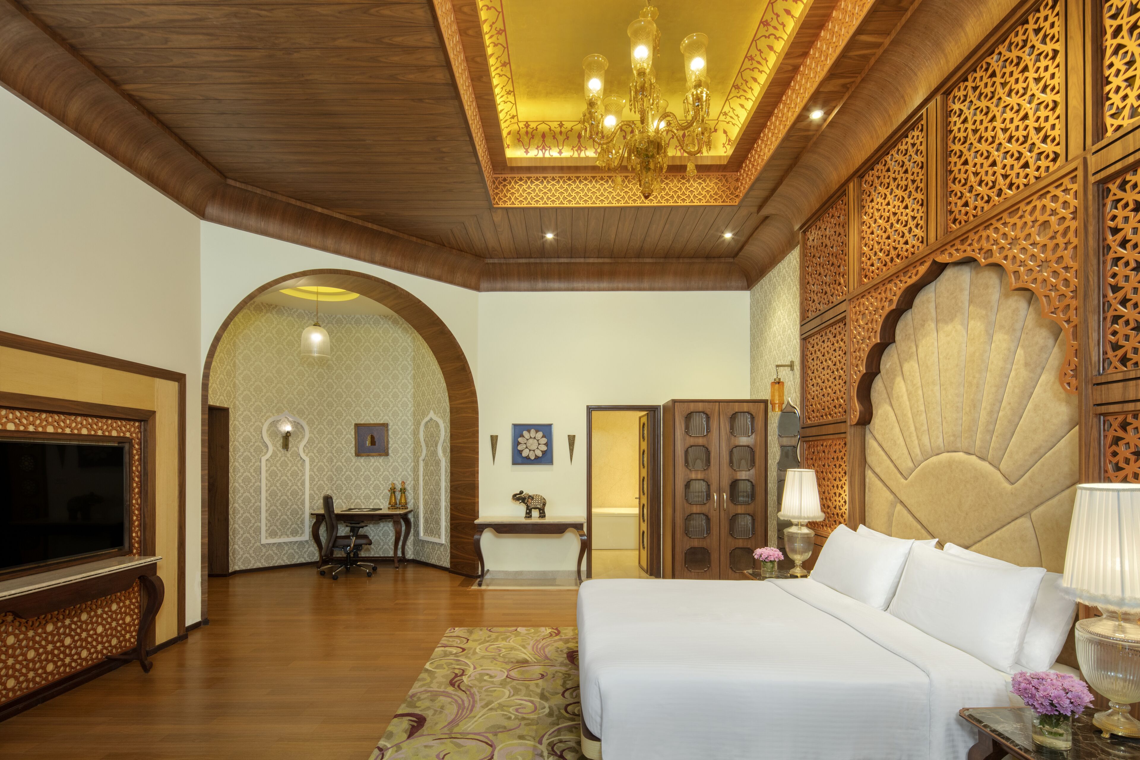 A hotel room with a large bed, a TV, a desk, and a decorative wall panel.