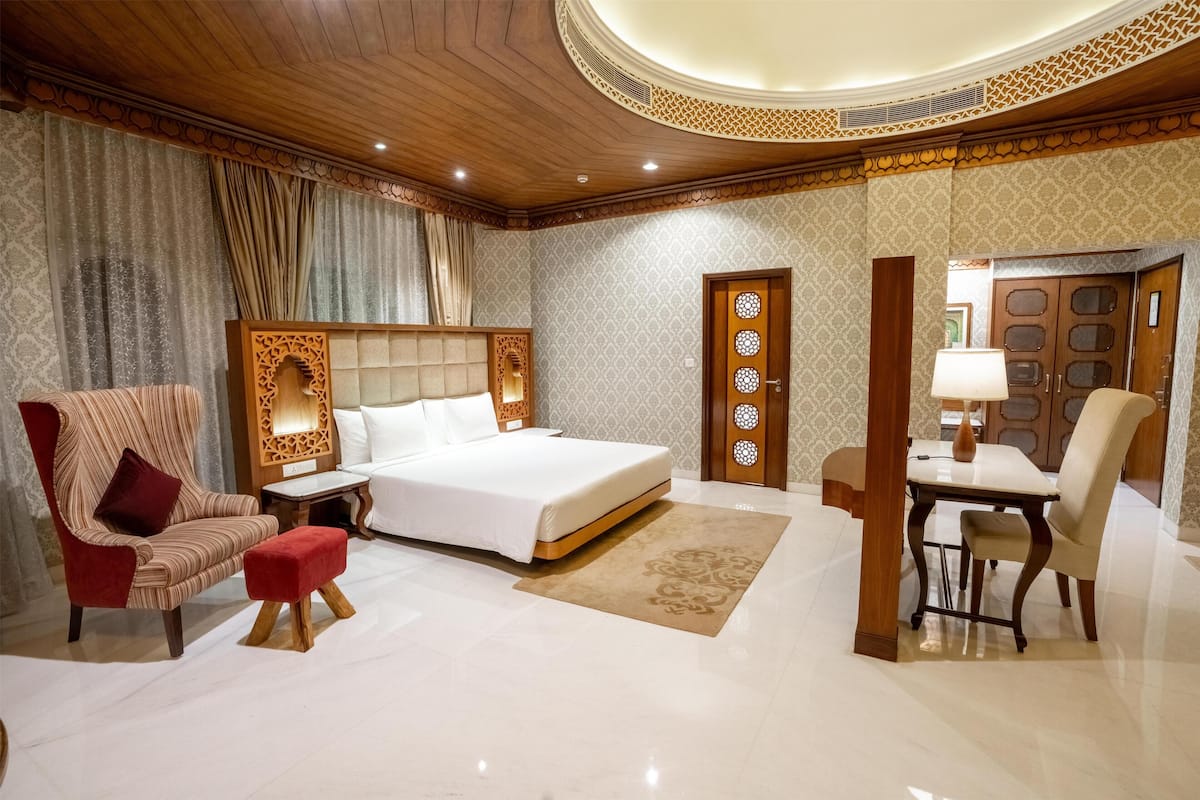 Ein Hotelzimmer mit einem großen Bett, einem roten Sessel, einem Holztisch und einem Essbereich.