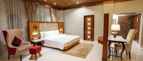 Una habitación de hotel con una cama grande, un sillón rojo, un escritorio de madera y un área de comedor.