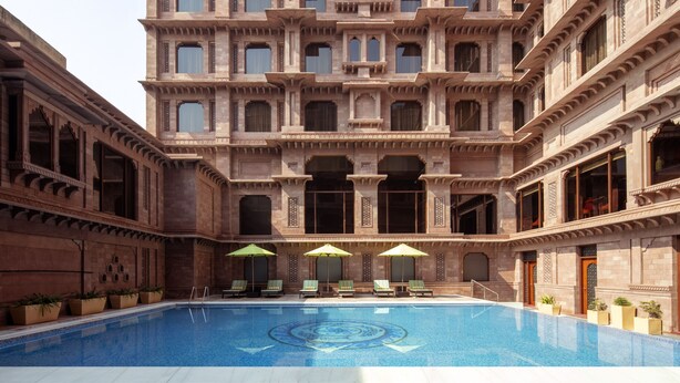 A pool area with a large pool, green umbrellas, and lounge chairs. - Radisson Hotel Jodhpur (Jodhpur)
