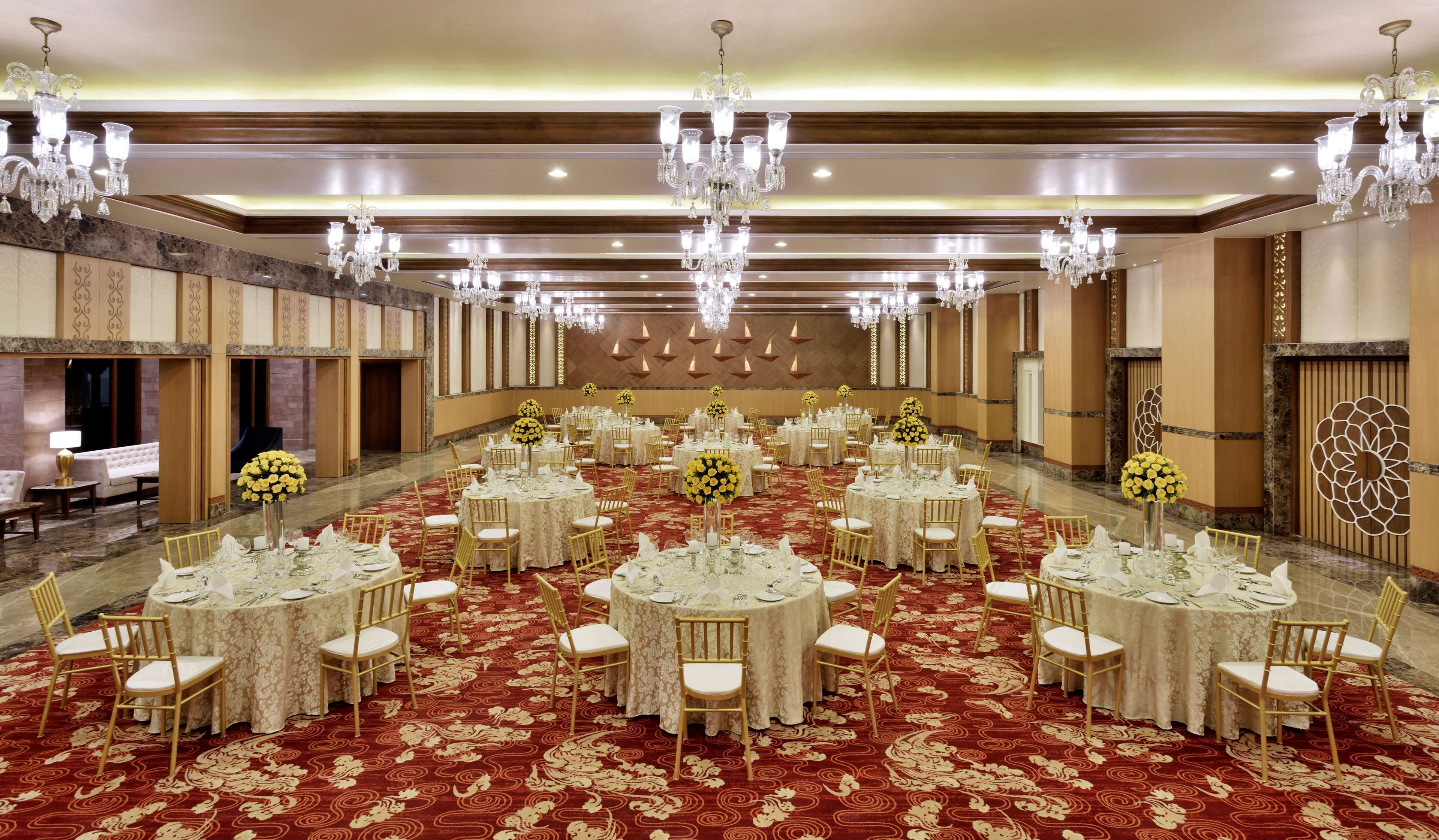 Una sala de banquetes amb taules rodones, cadirees daurades i lluminàries penjants.