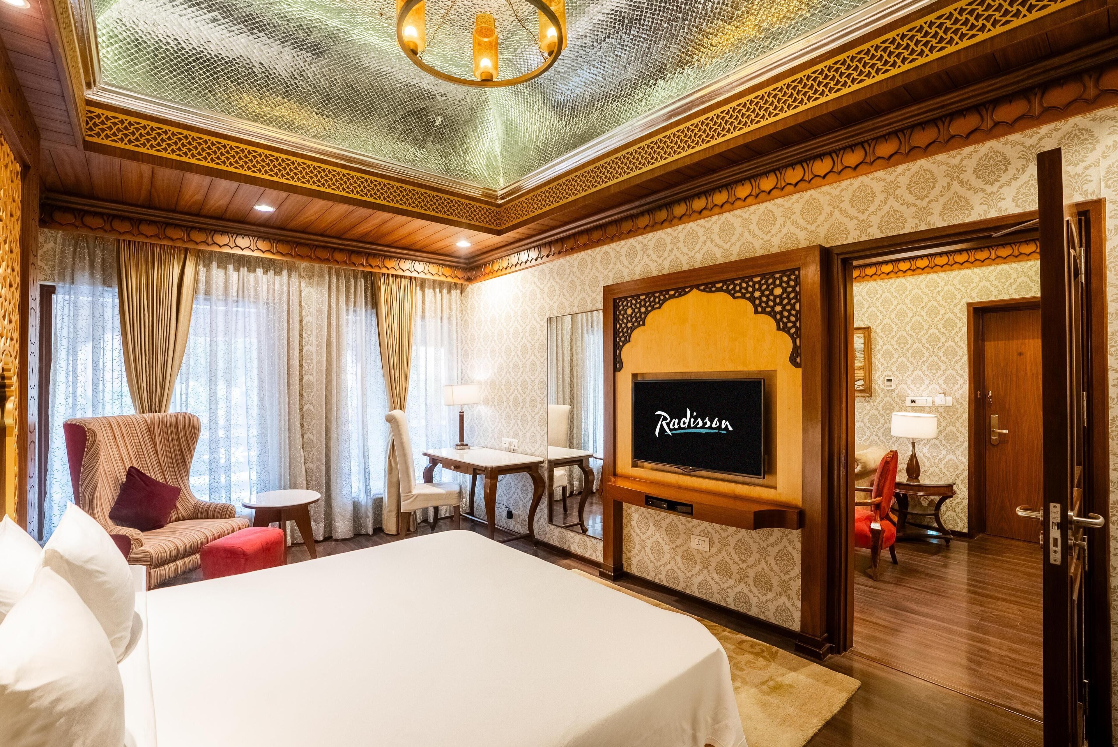 Una habitación de hotel con una cama grande, televisión, una mesita y una silla.