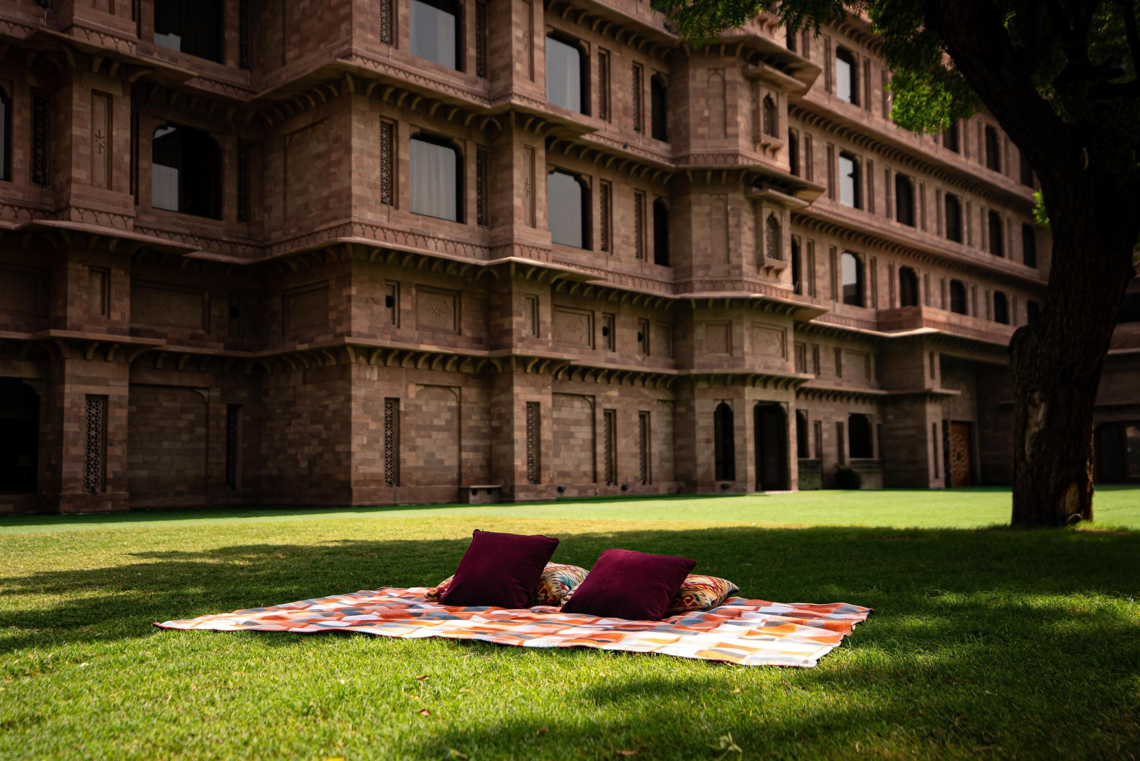 A building with multiple balconies and windows, a grassy lawn, and a blanket with pillows on it.