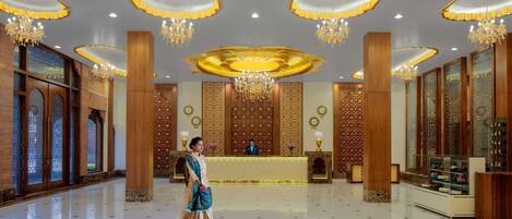 A spacious lobby with chandeliers, a reception desk, and a person walking.