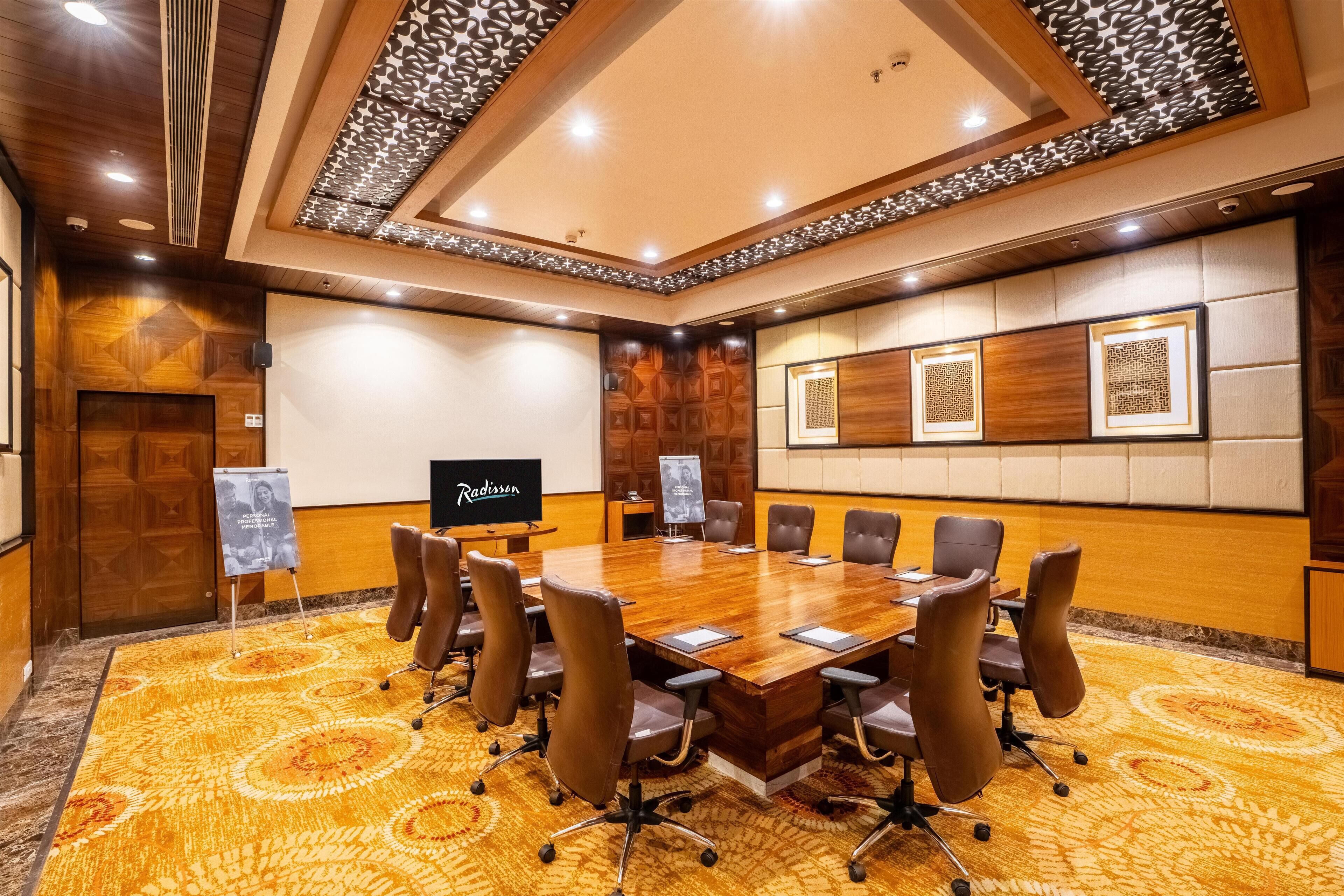 A conference room with a large wooden table, multiple chairs, and a television screen.