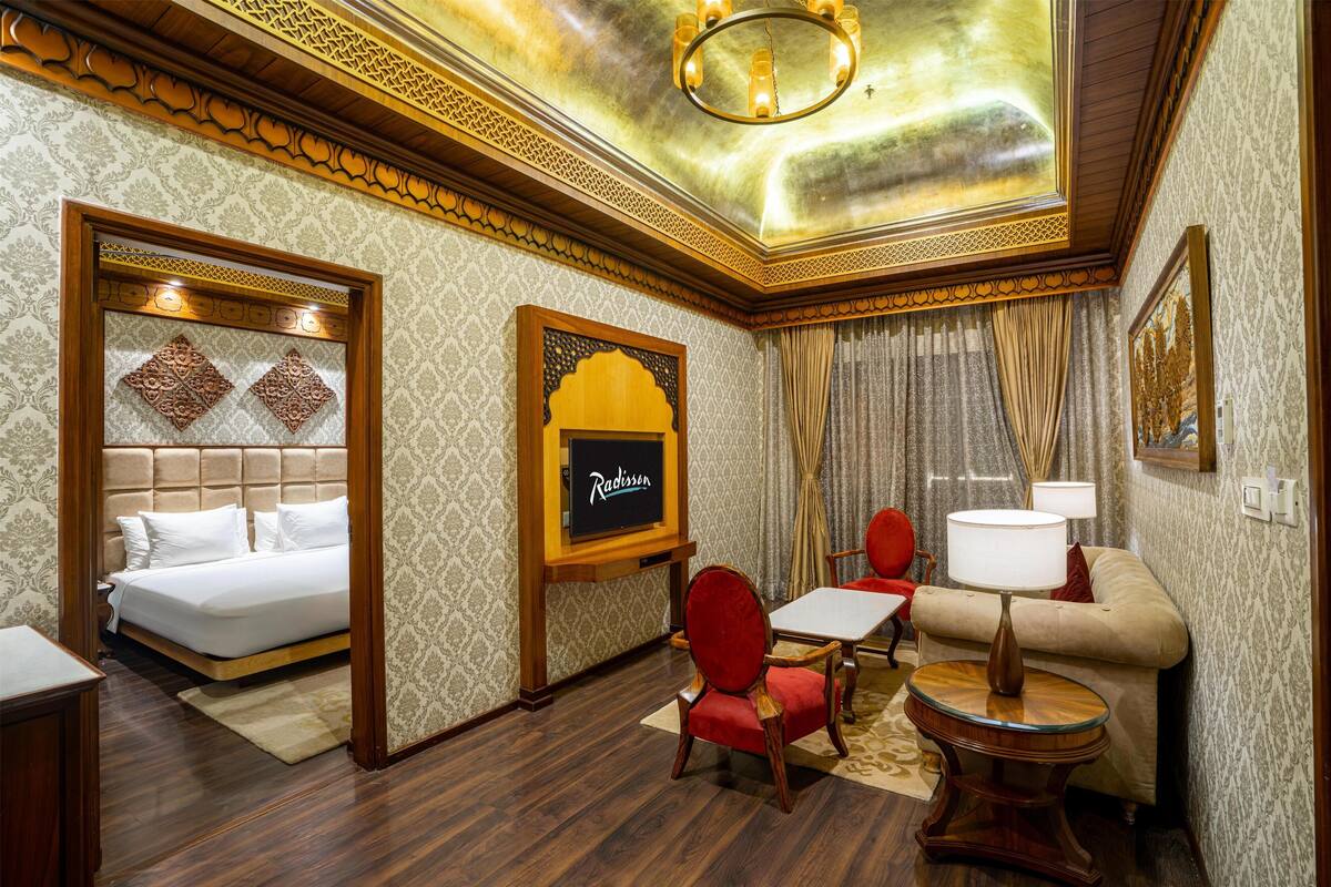 Ein Hotelzimmer mit einem Bett, einem roten Sessel, einer Couch, einem kleinen Tisch und einer Kristallleuchtre.