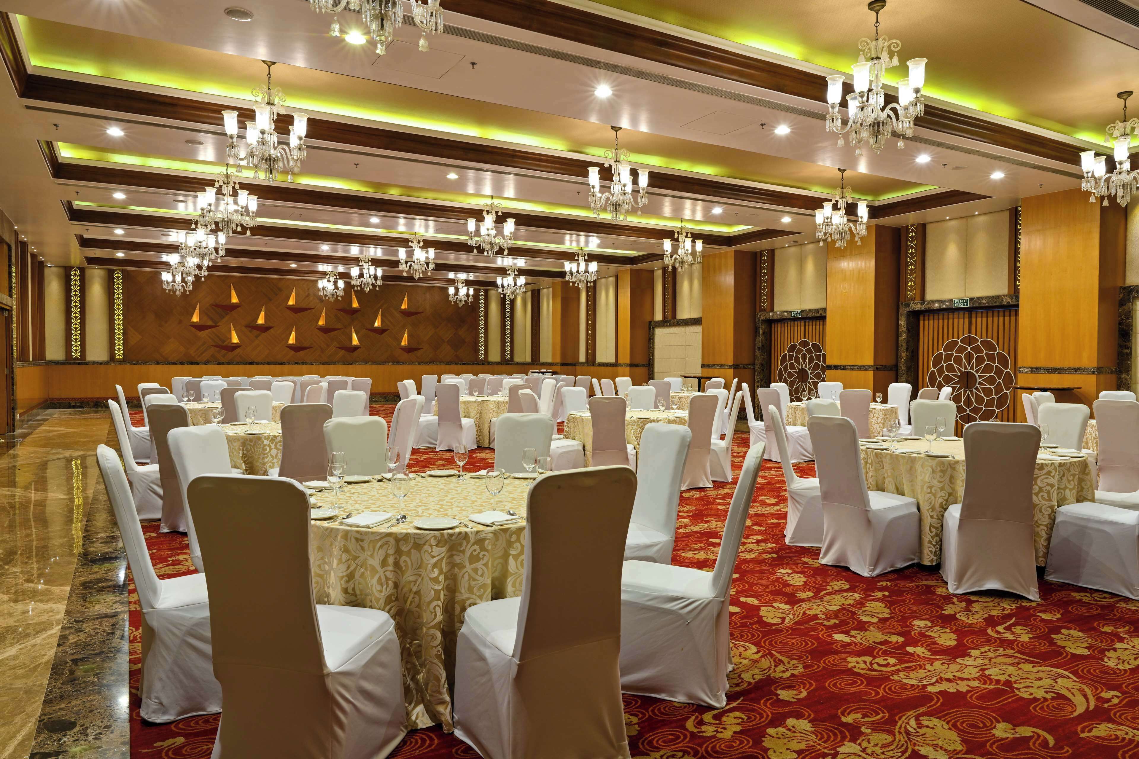 A banquet hall with round tables, white chairs, chandeliers, and a red carpet.