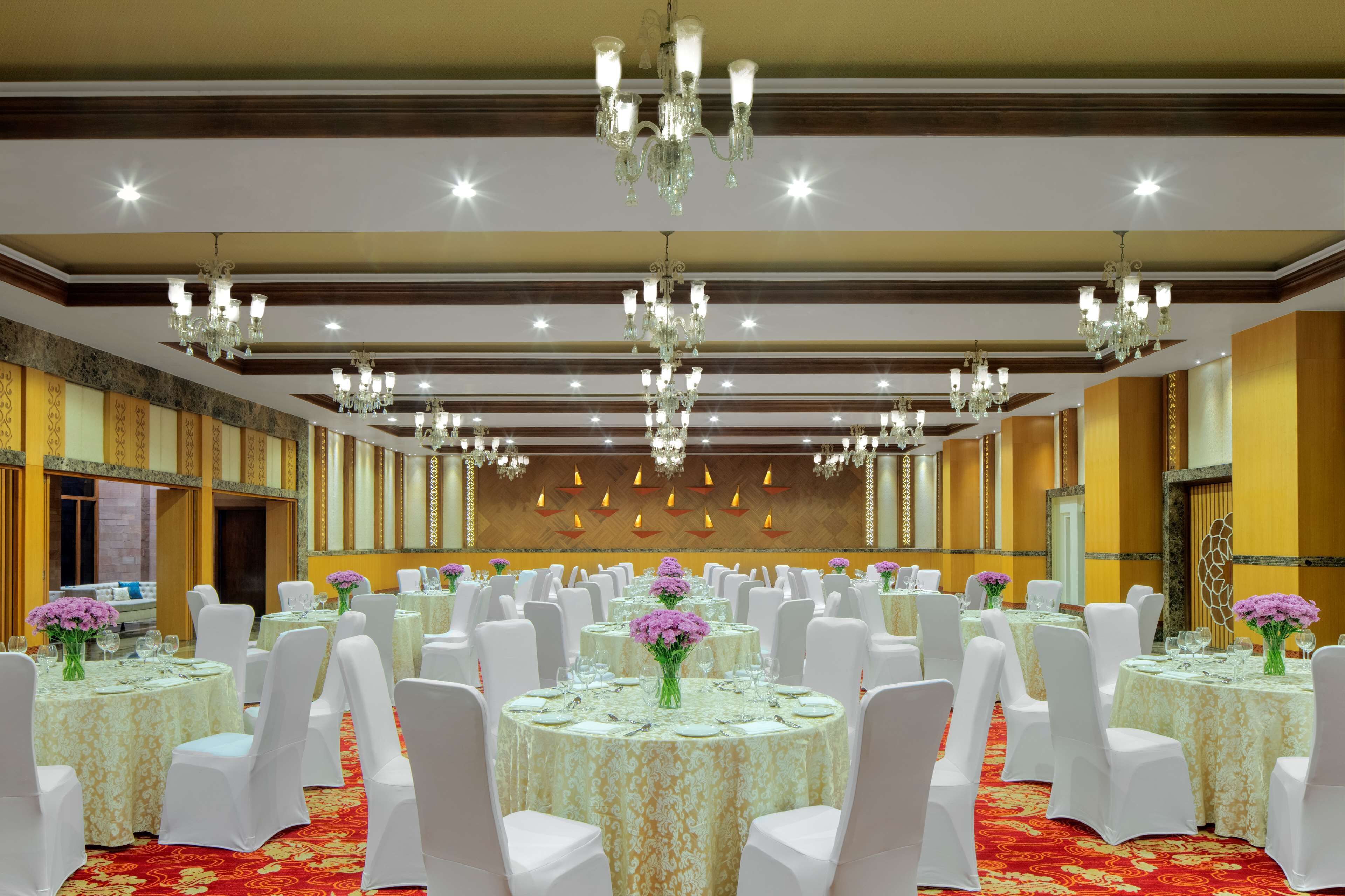 A banquet hall with round tables, white chairs, chandeliers, and floral centerpieces.