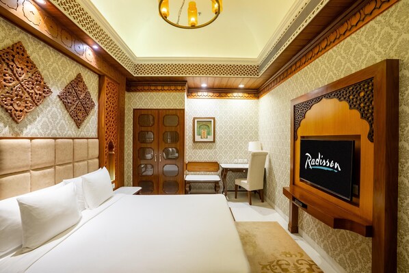 Habitación de hotel con una cama grande, un escritorio, una silla y un televisor en la pared.