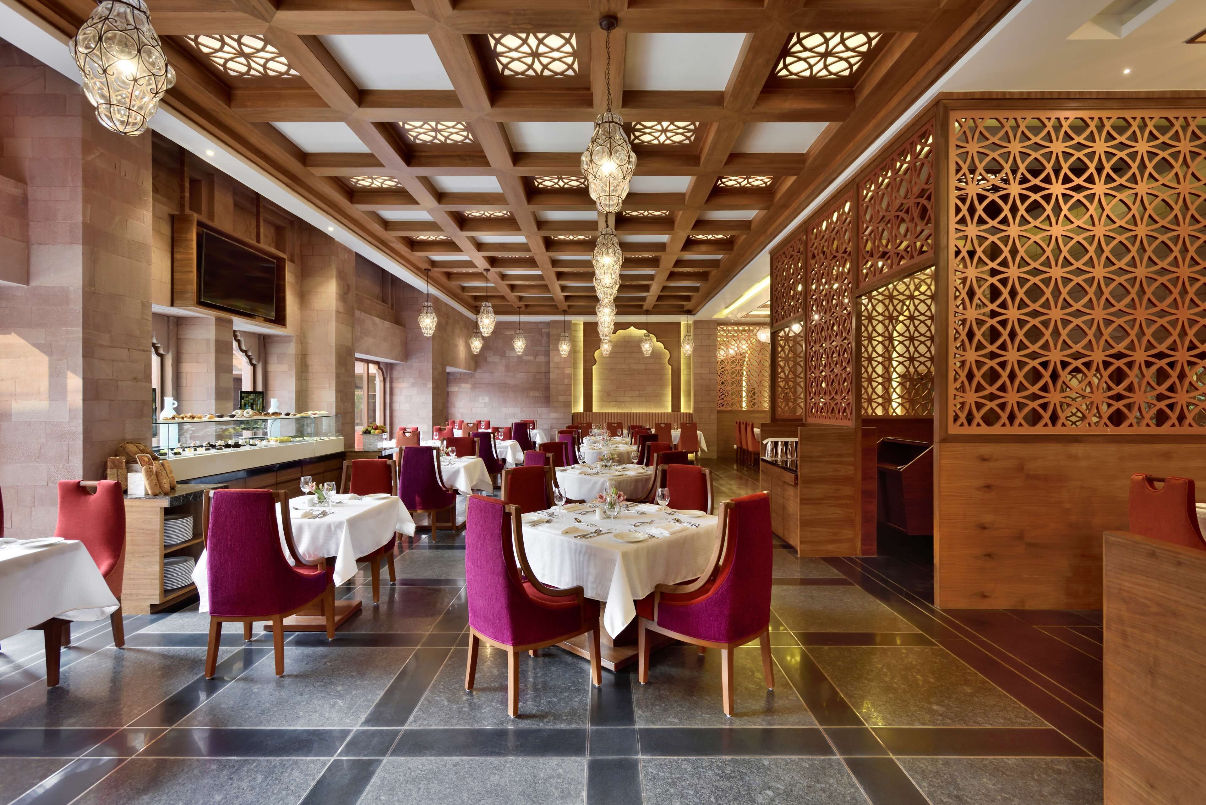 A restaurant with multiple tables, red chairs, and a wooden ceiling with intricate designs.