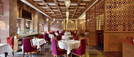 A restaurant with multiple tables, red chairs, and a wooden ceiling with intricate designs.