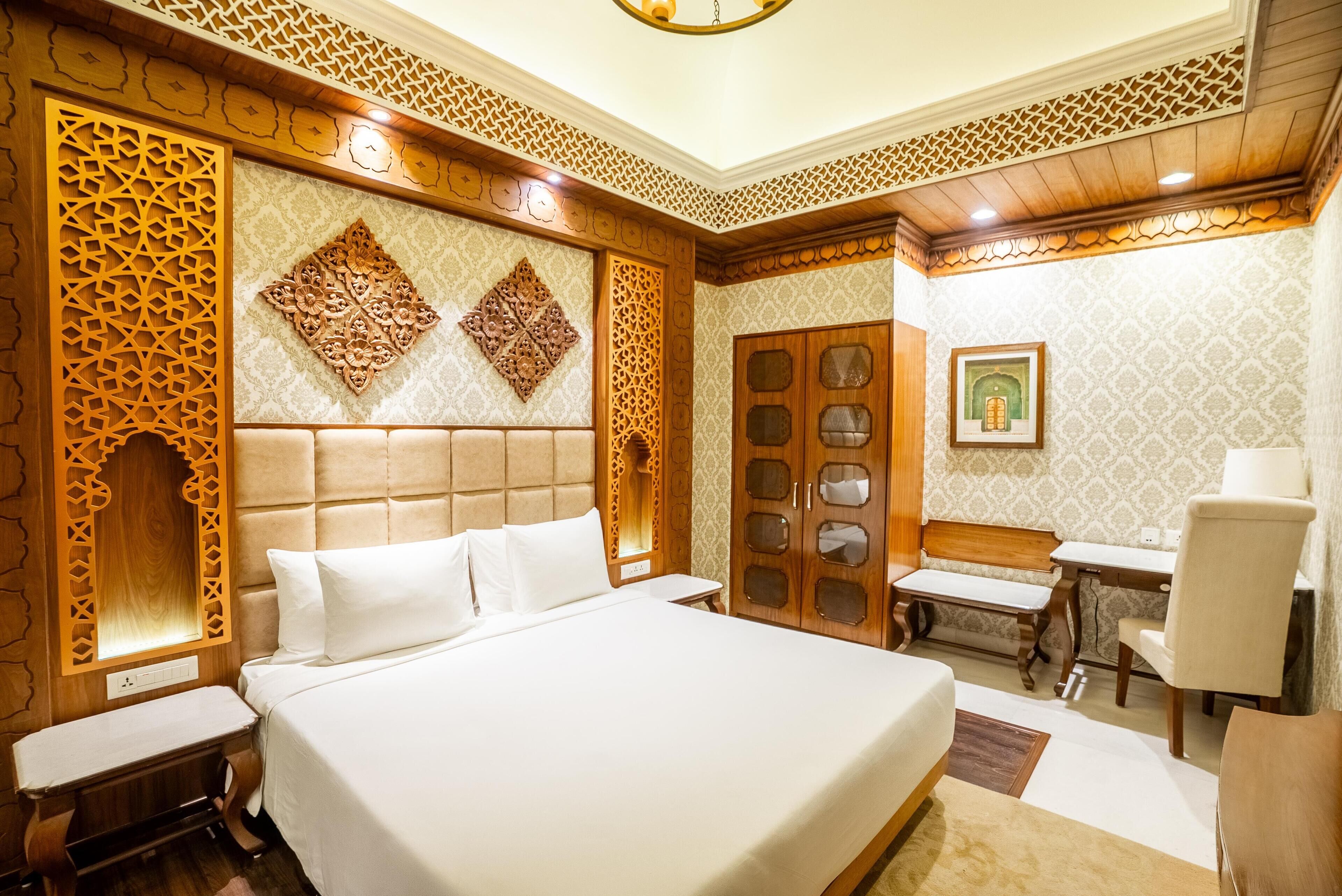 A hotel room with a large bed, a wooden wardrobe, a desk, and a chair.