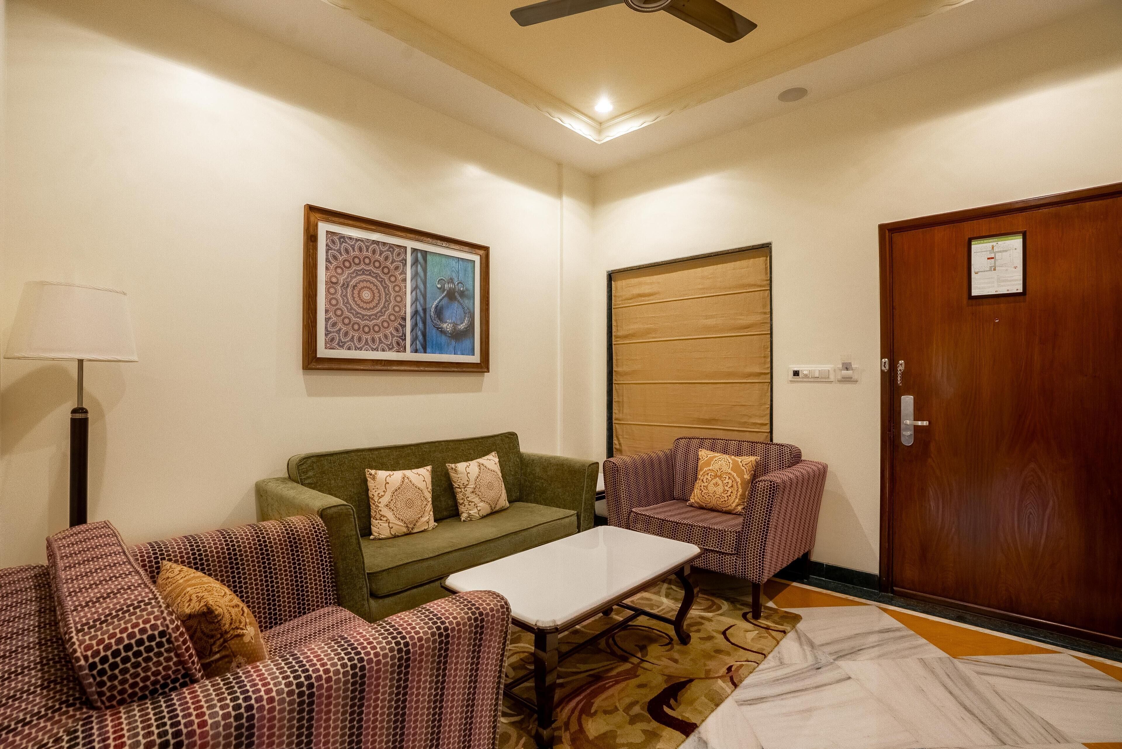 Una habitación con un sofá verde, sillones estampados, una mesa de centro blanca y una puerta de madera.