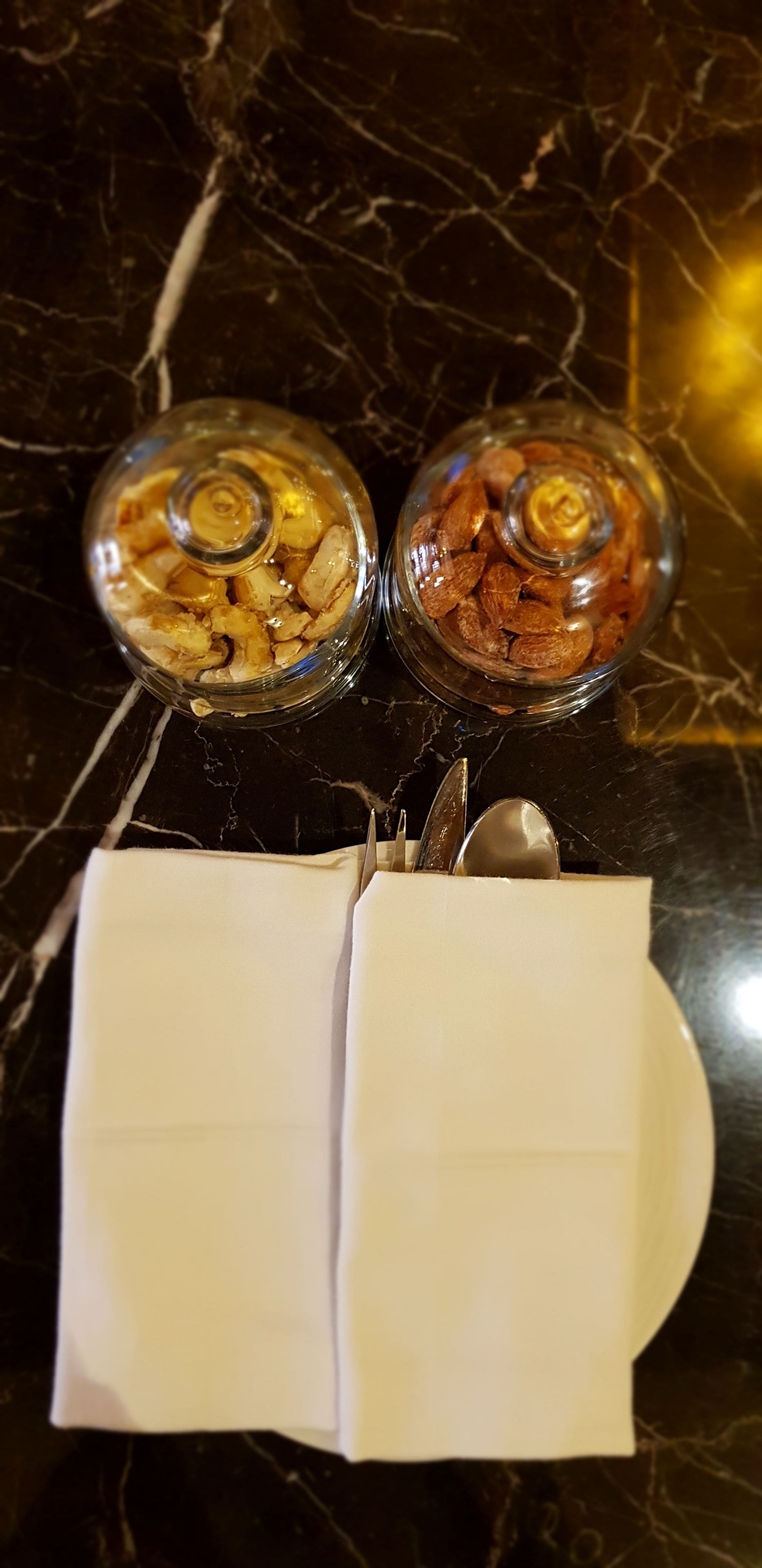Dos recipientes de vidrio con frutas secas sobre una superficie de mármol, una cuchara y una servilleta.