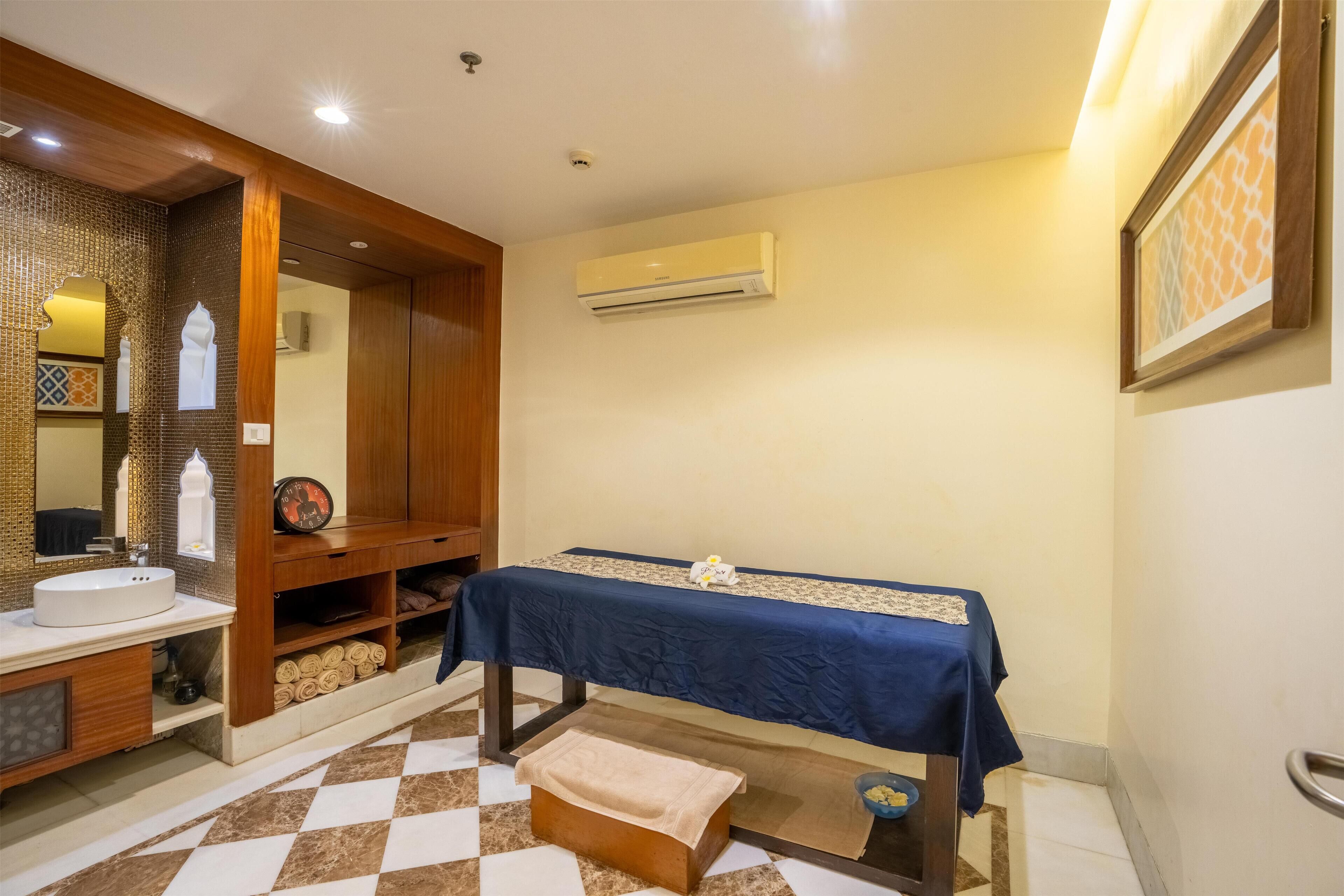 A bathroom with a sink, mirror, towel rack, and a massage table.