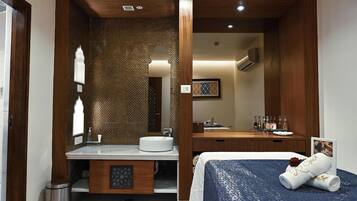 A hotel room with a wooden vanity, a round sink, a mirror, a bed with a blue bedspread, and a framed photo on the wall.