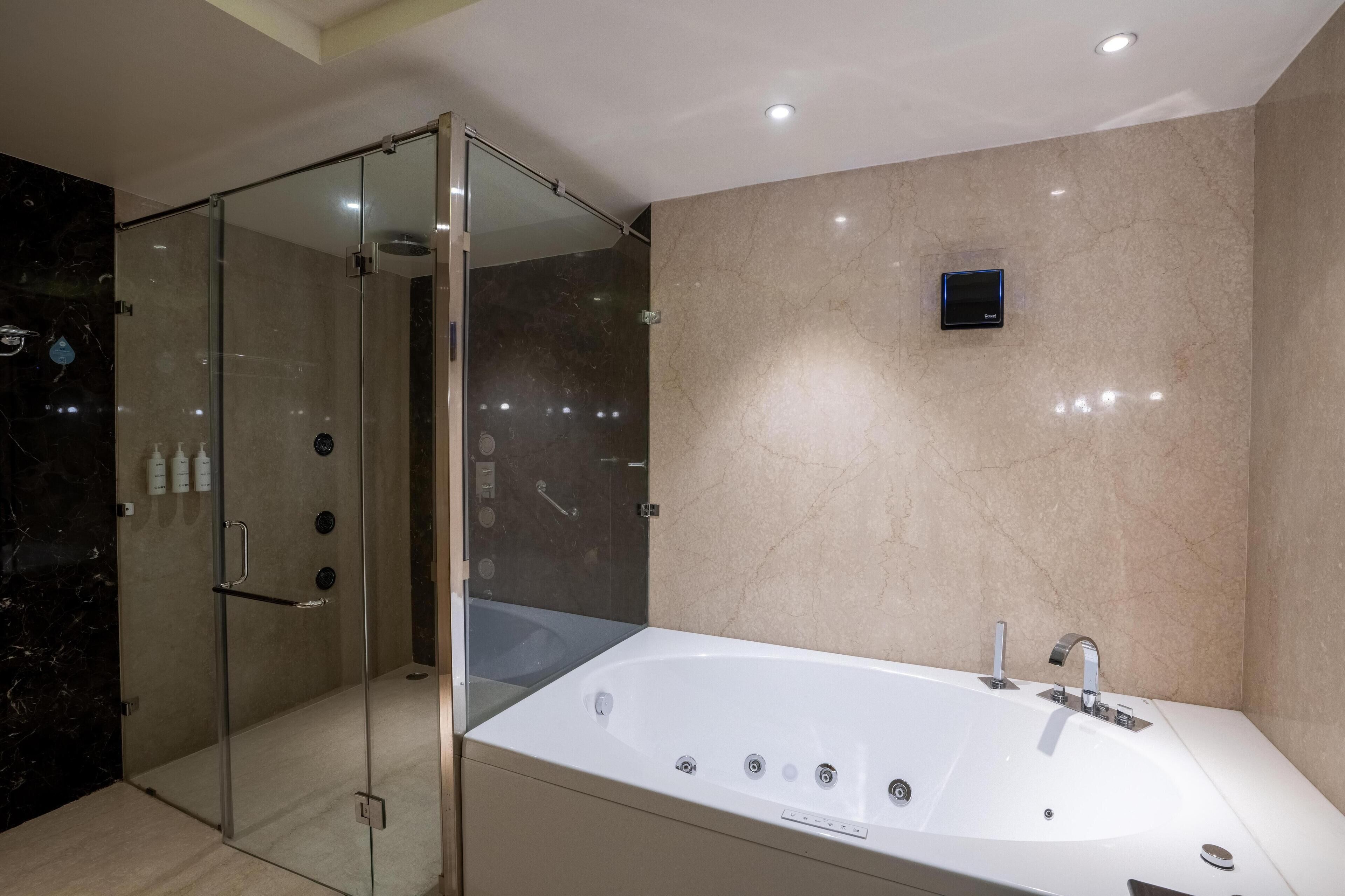 A modern bathroom with a glass-enclosed shower, a large white bathtub, and a wall-mounted TV.