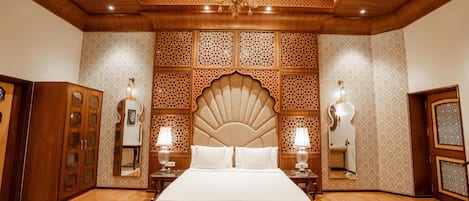 Un dormitorio espacioso con una cama grande, techo de madera, paneles decorativos en la pared y dos mesitas de noche con lámparas.