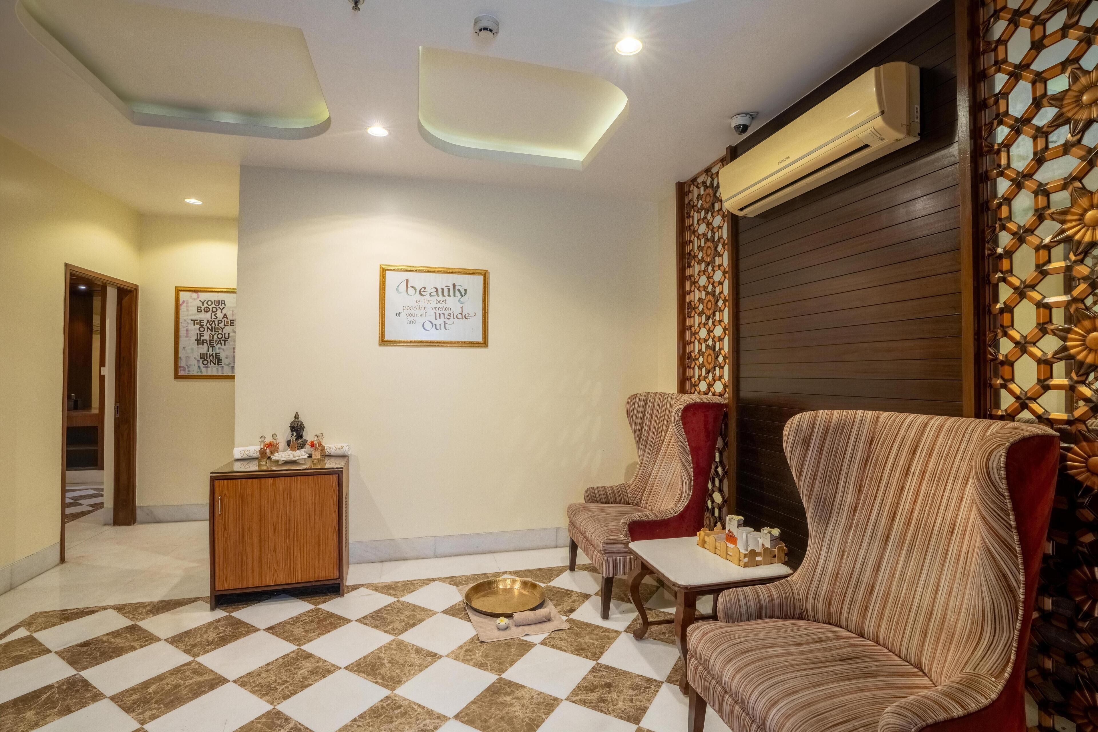 Un vestíbulo de hotel con suelo de cuadros, dos sillones a rayas, una pequeña mesa de madera, un panel decorativo y una unidad de aire acondicionado.