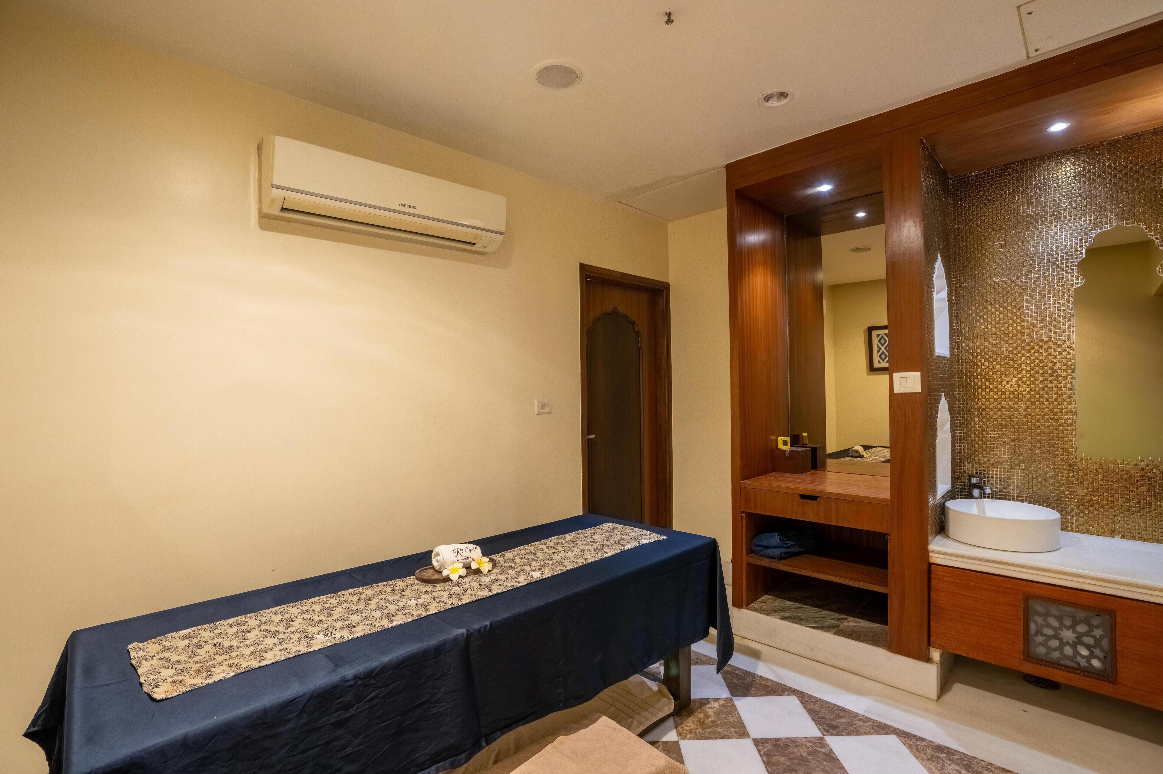 A room with a table covered by a dark cloth, an air conditioning unit on the wall, and a wooden vanity with a mirror.