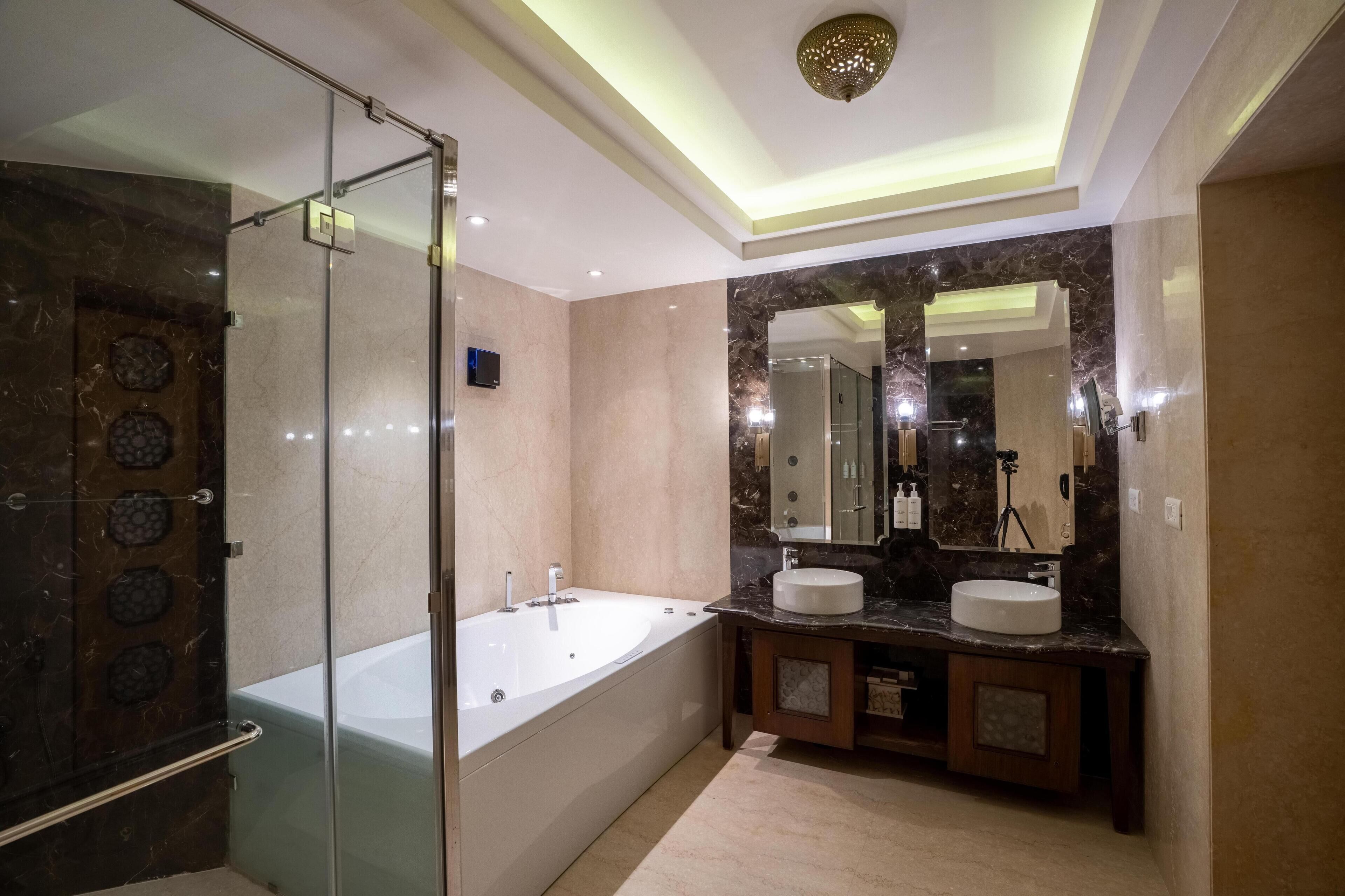Un baño moderno con ducha de vidrio, bañera independiente y tocador con dos lavamanos.