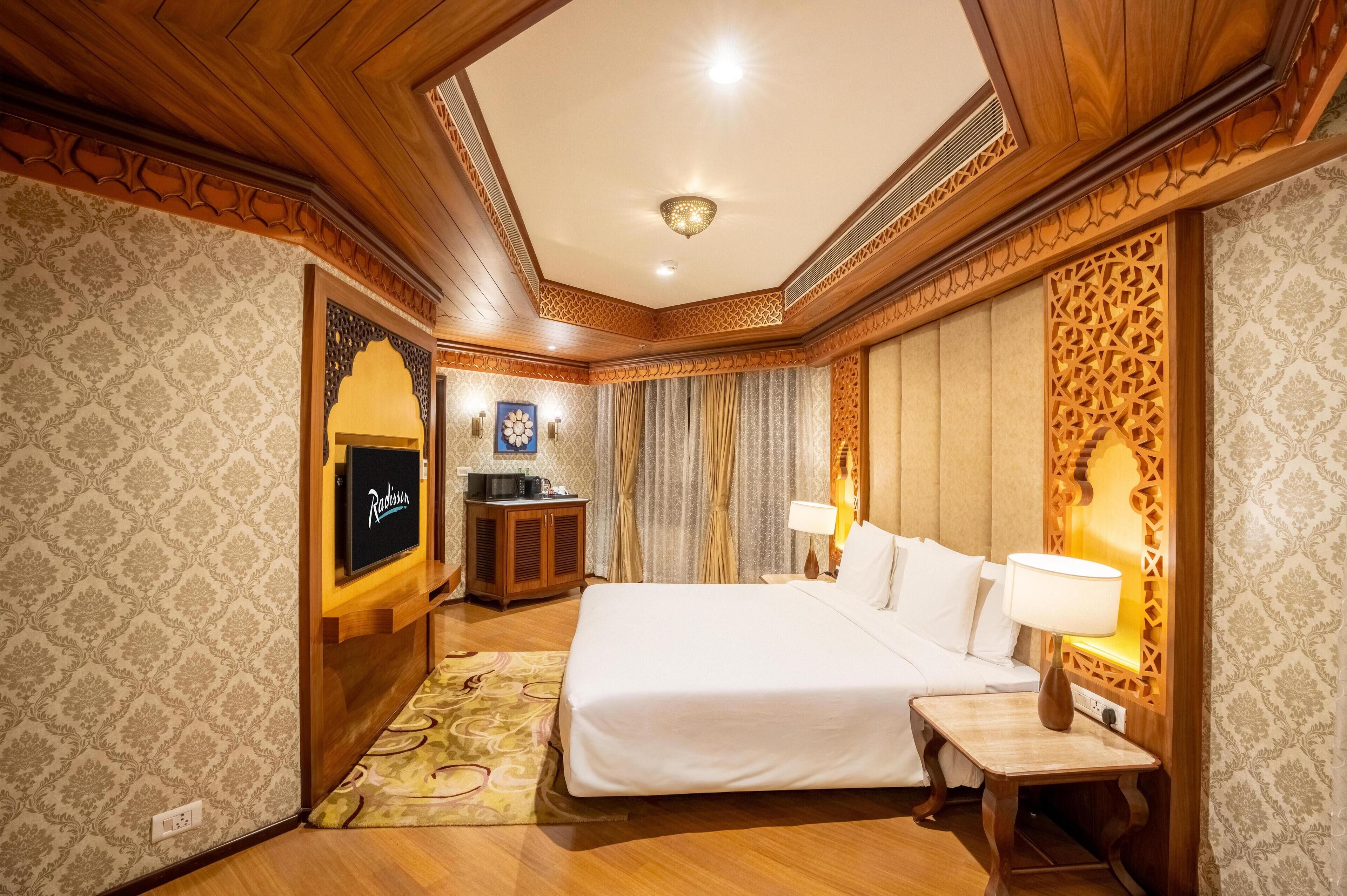 Une chambre d’hôtel avec un grand lit, une table de chevet avec une lampe, un téléviseur posé sur un meuble et un panneau décoratif au mur.