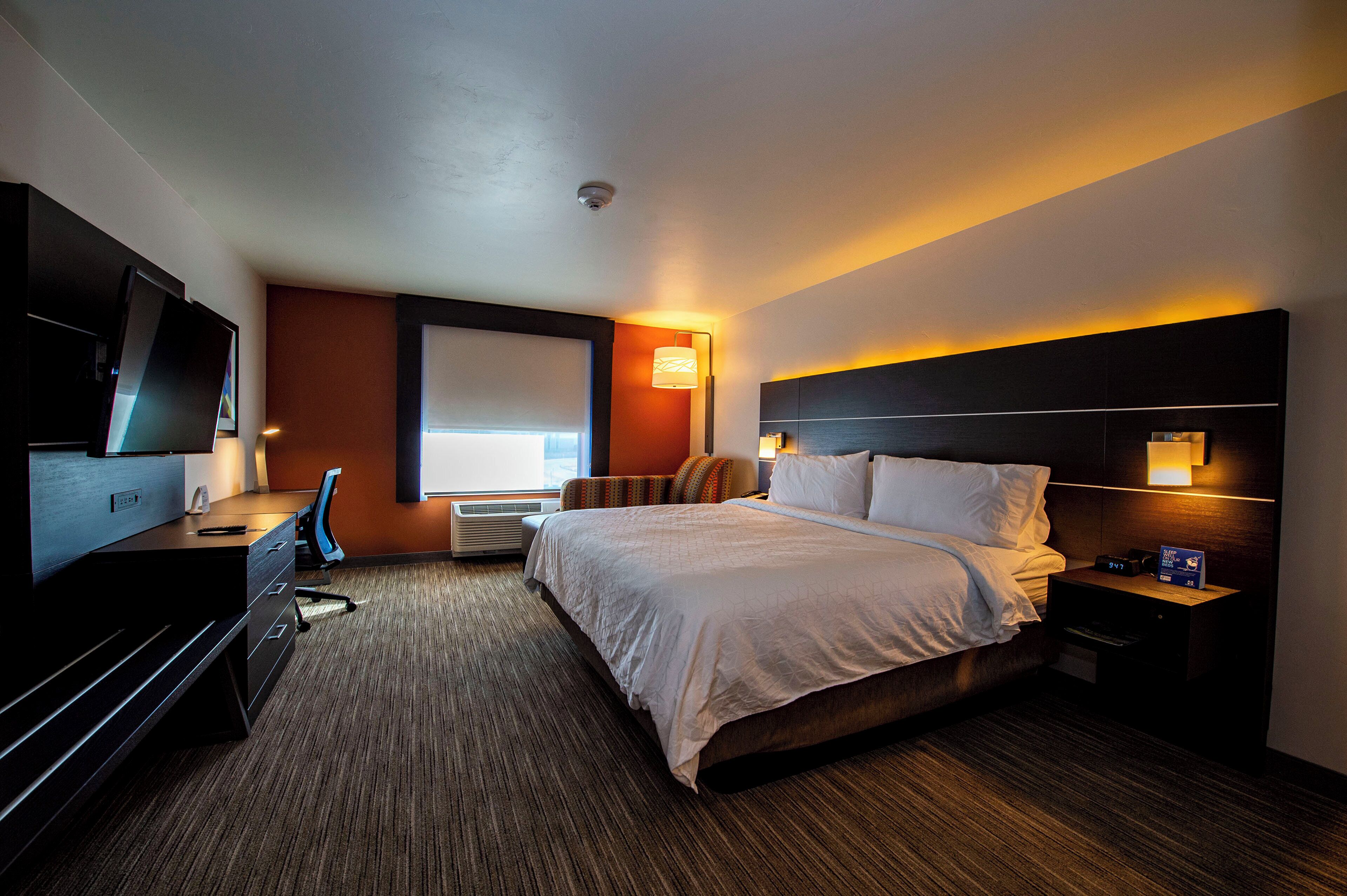 A hotel room with a bed, desk, chair, TV, and a window.