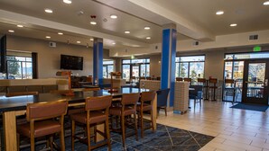 A spacious indoor area with a bar and seating area, large windows, and a flat-screen TV mounted on the wall. - Holiday Inn Express & Suites Colorado Springs AFA Northgate by IHG (Colorado Springs)